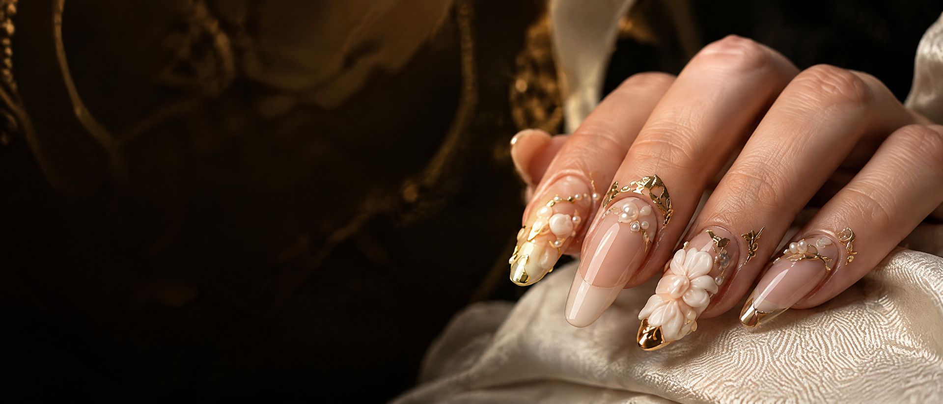 Almond nails with pearl, gold-leaf and 3D flower art resting on cream satin